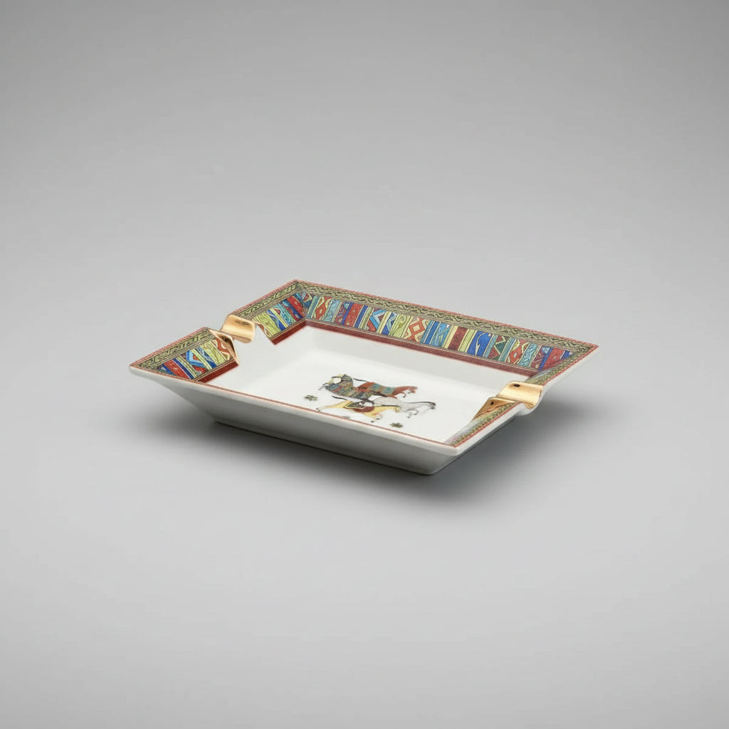 A rectangular ceramic ashtray with a white center and a highly decorative, colorful geometric border. The center features a painted illustration of two horse riders.