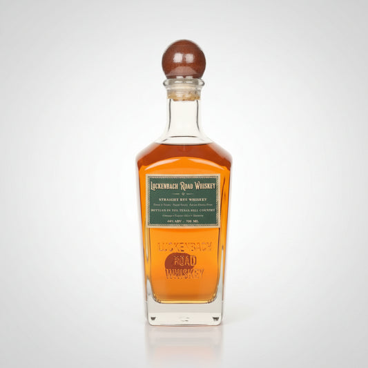 A bottle of Luckenbach Rye Road Whiskey with amber liquid, a green label, and a brown wooden stopper, shown on a white background.