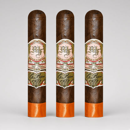 Three dark brown cigars standing upright side by side on a light gray background. Each cigar has a decorative cream, green, and red band label reading 'DH' and 'La Royale 1925', with a bright orange band at the bottom.