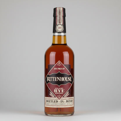 A bottle of Rittenhouse Straight Rye Whiskey on a white background with a soft reflection. The amber liquid inside the clear glass bottle is visible, along with a dark brown and beige label and a gold neck seal.