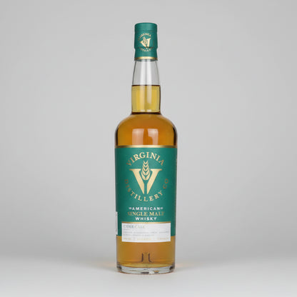 A bottle of Virginia Millery American Single Malt Whisky with a green label and gold liquid inside, shown on a white background with a reflection.