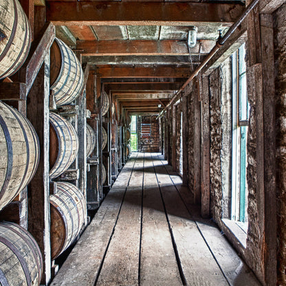 Whiskey barrels stacked in a warehouse with stone walls and wooden floor.