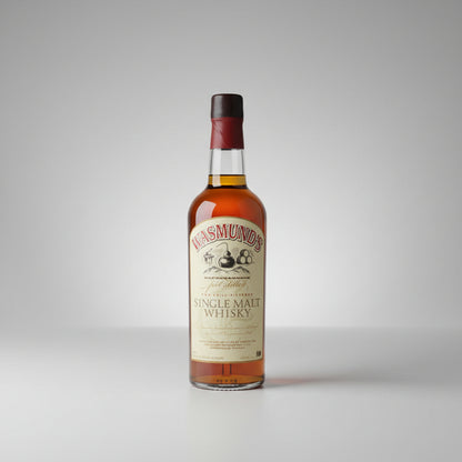 A bottle of Masmund's Single Malt Whisky standing on a stone outdoors with a blurred green forest background.